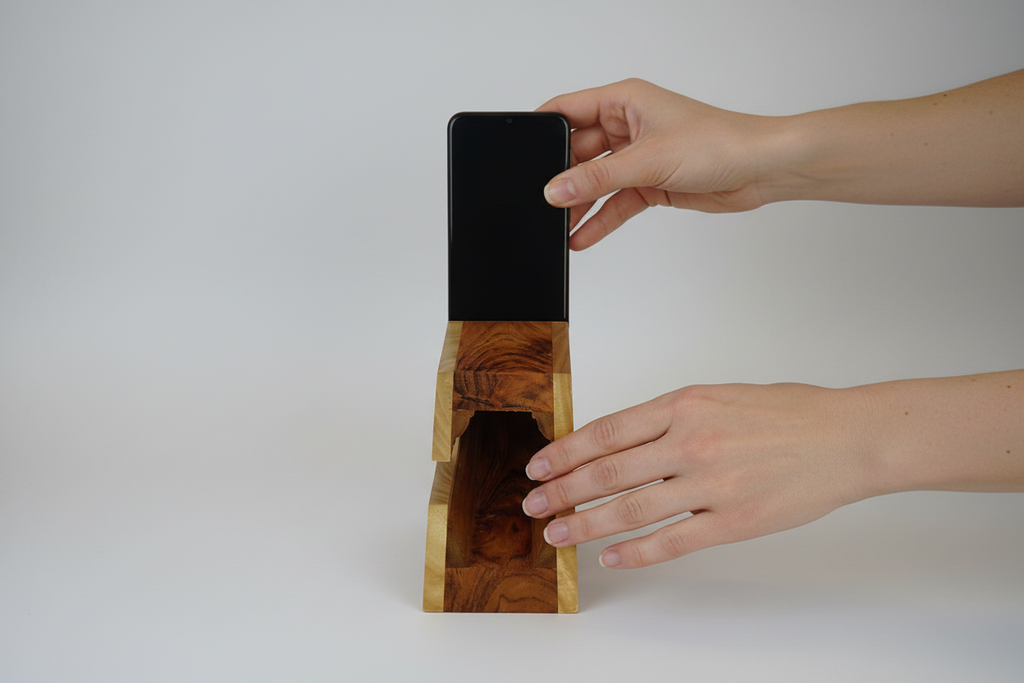 Person using a wooden phone stand with a black phone on a white background