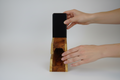 Person using a wooden phone stand with a black phone on a white background