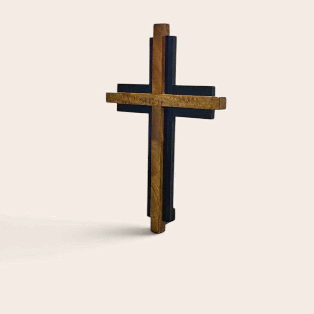 A double-layered wooden cross with a natural brown wood grain outer layer and a dark walnut inner layer, standing upright against a light beige background.
