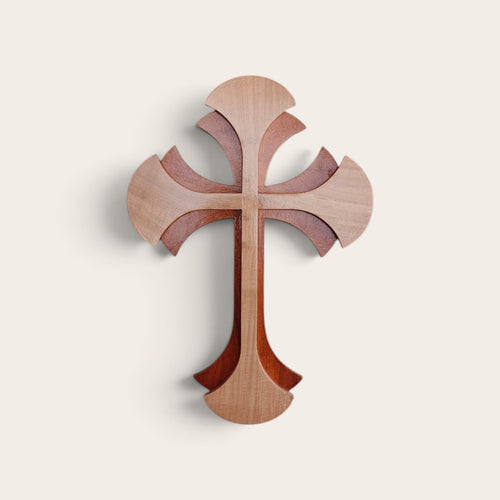 A decorative wooden wall cross with layered, scalloped cutouts in three natural wood tones, shown against a solid off-white background.