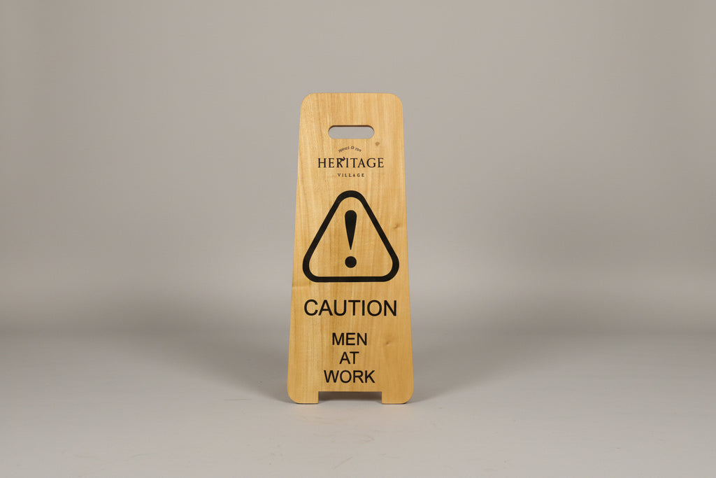 Wooden sign with 'Caution: Men at Work' on a white surface next to a wooden cabinet.