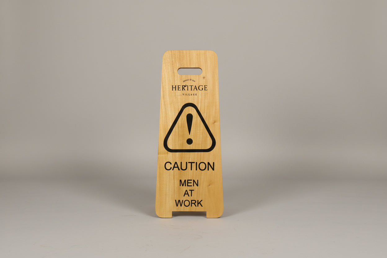Wooden sign with 'Caution: Men at Work' on a white surface next to a wooden cabinet.